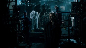 Movie still from “Ganglands” (2021), created by Julien Leclercq – A group of people standing around in a dark room; Wide shot, Over the shoulder angle