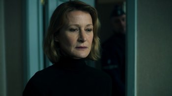 Movie still from “Ganglands” (2021), created by Julien Leclercq – A woman in a black shirt is standing in front of a door; Close Up shot, Over the shoulder angle