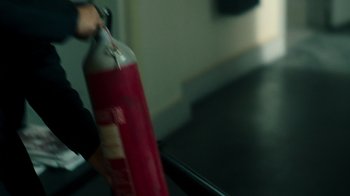 Movie still from “Ganglands” (2021), created by Julien Leclercq – A person holding a fire extinguisher in a room; Close Up shot, Over the shoulder angle