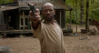 Movie still from “Get on Up” (2014), directed by Tate Taylor – A man holding a gun in front of a house; Medium shot, Low angle
