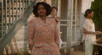 Movie still from “Get on Up” (2014), directed by Tate Taylor – An older woman in an orange floral dress stands in front of an old house; Medium shot, Over the shoulder angle