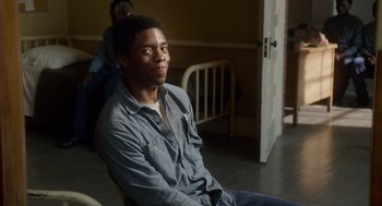 Movie still from “Get on Up” (2014), directed by Tate Taylor – A man sitting on a chair in a room; Medium shot, Over the shoulder angle