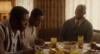 Movie still from “Get on Up” (2014), directed by Tate Taylor – A group of people sitting at a table eating food; Medium shot, Over the shoulder angle