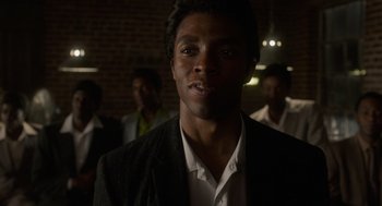 Movie still from “Get on Up” (2014), directed by Tate Taylor – A man in a suit and tie standing in front of a group of men; Close Up shot, Low angle