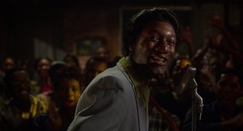 Movie still from “Get on Up” (2014), directed by Tate Taylor – A man with a microphone in front of a group of people; Close Up shot, Over the shoulder angle
