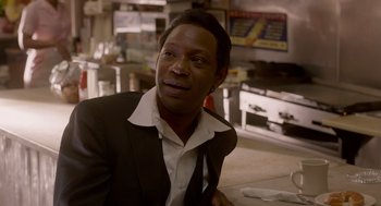 Movie still from “Get on Up” (2014), directed by Tate Taylor – A man in a suit sitting at a table in front of a stove; Close Up shot, Over the shoulder angle