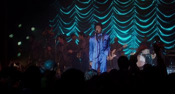 Movie still from “Get on Up” (2014), directed by Tate Taylor – A man in a blue suit singing into a microphone on a stage; Wide shot, High angle