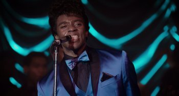 Movie still from “Get on Up” (2014), directed by Tate Taylor – A man in a blue suit and bow tie singing into a microphone; Close Up shot, Low angle