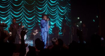 Movie still from “Get on Up” (2014), directed by Tate Taylor – A man in a blue suit singing on a stage; Wide shot, Over the shoulder angle