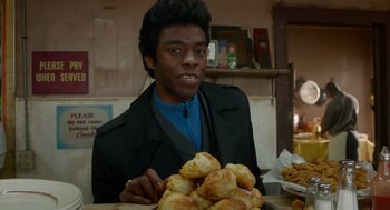 Movie still from “Get on Up” (2014), directed by Tate Taylor – A man sitting in front of a pile of biscuits; Close Up shot, Over the shoulder angle
