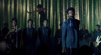 Movie still from “Get on Up” (2014), directed by Tate Taylor – A group of men standing next to each other on a stage; Medium shot, Over the shoulder angle