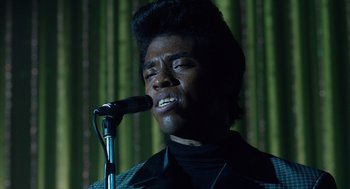 Movie still from “Get on Up” (2014), directed by Tate Taylor – A man in a black shirt is singing into a microphone; Close Up shot, Low angle