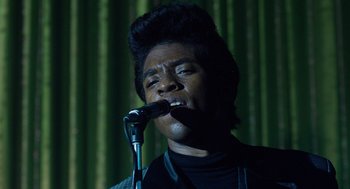 Movie still from “Get on Up” (2014), directed by Tate Taylor – A man is singing into a microphone in front of a green curtain; Close Up shot, Low angle