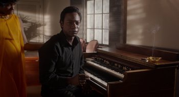 Movie still from “Get on Up” (2014), directed by Tate Taylor – A man sitting in front of a piano in a darkened room; Medium shot, High angle
