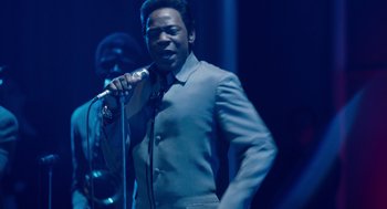 Movie still from “Get on Up” (2014), directed by Tate Taylor – A man holding a microphone in front of another man; Medium shot, Low angle