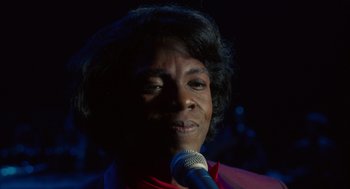 Movie still from “Get on Up” (2014), directed by Tate Taylor – A person holding a microphone in front of a dark background; Close Up shot, High angle