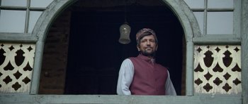 Movie still from “Haider” (2014), directed by Vishal Bhardwaj – A man standing in front of an archway with a clock hanging from the ceiling; Medium shot, Low angle
