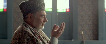 Movie still from “Haider” (2014), directed by Vishal Bhardwaj – An older man wearing a hat and praying with his hands; Close Up shot, Low angle