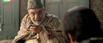 Movie still from “Haider” (2014), directed by Vishal Bhardwaj – An older man wearing a hat looking at his cell phone; Close Up shot, Over the shoulder angle