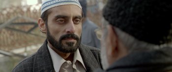 Movie still from “Haider” (2014), directed by Vishal Bhardwaj – A man with a beard wearing a hat and a suit; Close Up shot, Over the shoulder angle