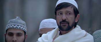 Movie still from “Haider” (2014), directed by Vishal Bhardwaj – A man with a beard wearing a white hat; Close Up shot, Over the shoulder angle