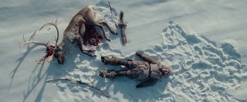 Movie still from “Hanna” (2011), directed by Joe Wright – A man laying in the snow next to a dead animal; Wide shot, Overhead angle