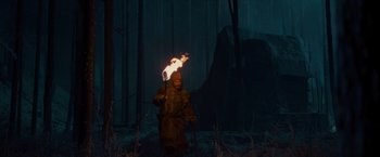 Movie still from “Hanna” (2011), directed by Joe Wright – A person holding a fire in a forest; Wide shot, Low angle