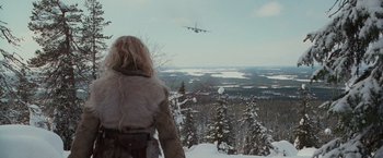 Movie still from “Hanna” (2011), directed by Joe Wright – A woman in a fur coat looking at an airplane flying in the sky; Extreme Wide shot, Over the shoulder angle