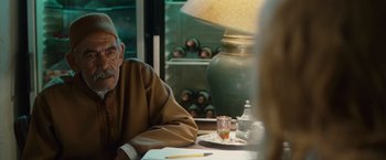 Movie still from “Hanna” (2011), directed by Joe Wright – An older man sitting at a table with a glass of wine; Close Up shot, Over the shoulder angle
