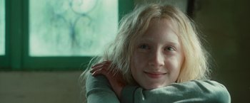Movie still from “Hanna” (2011), directed by Joe Wright – A young blonde girl smiling for the camera; Close Up shot, Over the shoulder angle
