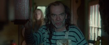 Movie still from “Hanna” (2011), directed by Joe Wright – A man with long black hair and striped shirt holding a paper bag; Medium shot, Over the shoulder angle