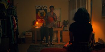 Movie still from “Heartbreak High” (2022), created by Michael Jenkins – A man holding a basketball in a room with posters on the wall; Wide shot, Over the shoulder angle