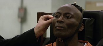 Movie still from “Black Mirror” (2011), created by Charlie Brooker – A man is putting on a fake head band; Close Up shot, High angle