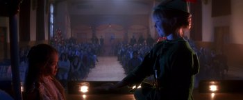 Movie still from “Hook” (1991), directed by Steven Spielberg – A woman standing in front of an audience at night; Wide shot, Over the shoulder angle