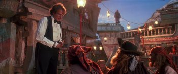 Movie still from “Hook” (1991), directed by Steven Spielberg – A man standing next to a man sitting on top of a boat; Wide shot, Over the shoulder angle