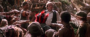 Movie still from “Hook” (1991), directed by Steven Spielberg – A man in a crowd of people wearing a red and black headdress; Medium shot, Over the shoulder angle