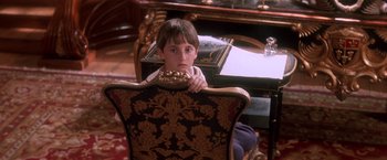 Movie still from “Hook” (1991), directed by Steven Spielberg – A young boy sitting in a chair in front of a desk; Medium shot, High angle