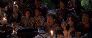 Movie still from “Hook” (1991), directed by Steven Spielberg – A group of people sitting around a table with a lit candle; Medium shot, High angle