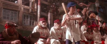 Movie still from “Hook” (1991), directed by Steven Spielberg – A group of baseball players sitting next to each other holding a bat; Medium shot, Low angle