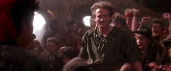 Movie still from “Hook” (1991), directed by Steven Spielberg – A group of people gathered around a man in a green shirt; Medium shot, Over the shoulder angle