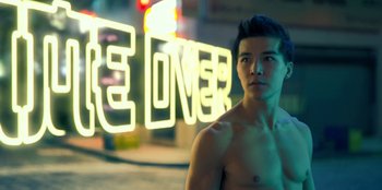 Movie still from “Black Mirror” (2011), created by Charlie Brooker – A man standing in front of a neon light sign; Medium shot, Over the shoulder angle