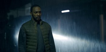 Movie still from “Black Mirror” (2011), created by Charlie Brooker – A man standing in the rain in a green jacket; Medium shot, Low angle
