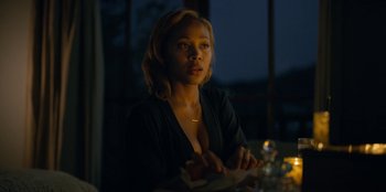 Movie still from “Black Mirror” (2011), created by Charlie Brooker – A woman sitting at a table in a dark room; Close Up shot, Over the shoulder angle