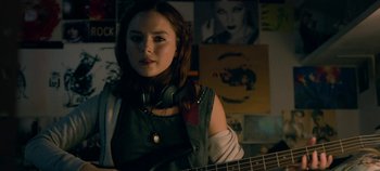 Movie still from “Black Mirror” (2011), created by Charlie Brooker – A woman with a guitar in a room with pictures on the wall; Medium shot, Over the shoulder angle