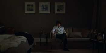 Movie still from “Black Mirror” (2011), created by Charlie Brooker – A man sitting on a chair in a living room; Wide shot, Over the shoulder angle