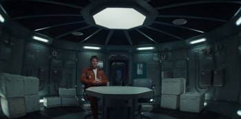 Movie still from “Black Mirror” (2011), created by Charlie Brooker – A man sitting at a table in a room; Wide shot, High angle