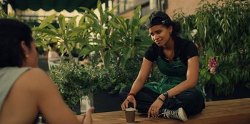 Movie still from “Black Mirror” (2011), created by Charlie Brooker – A woman sitting on the ground with a cup of coffee; Medium shot, Over the shoulder angle