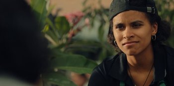 Movie still from “Black Mirror” (2011), created by Charlie Brooker – A woman wearing a black shirt and a black hat; Close Up shot, Over the shoulder angle