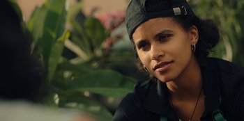 Movie still from “Black Mirror” (2011), created by Charlie Brooker – A woman wearing a black hat is looking at the camera; Close Up shot, Over the shoulder angle