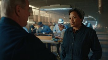 Movie still from “A League of Their Own” (2022), created by Abbi Jacobson – A woman standing next to a crowd of people in a room; Medium shot, Over the shoulder angle
